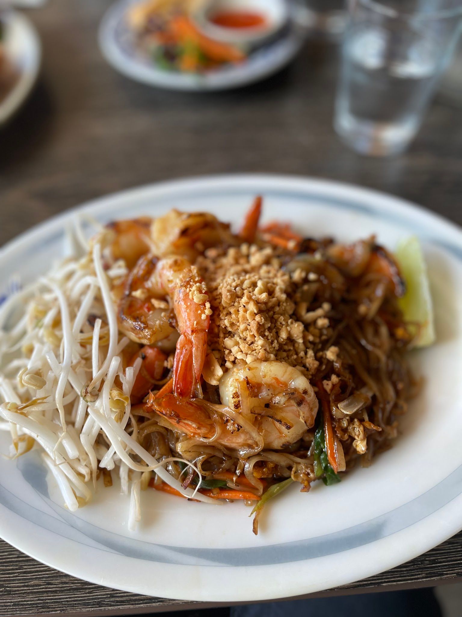 Prawn pad thai with crushed peanuts and bean sprouts on a white plate in a restaurant setting