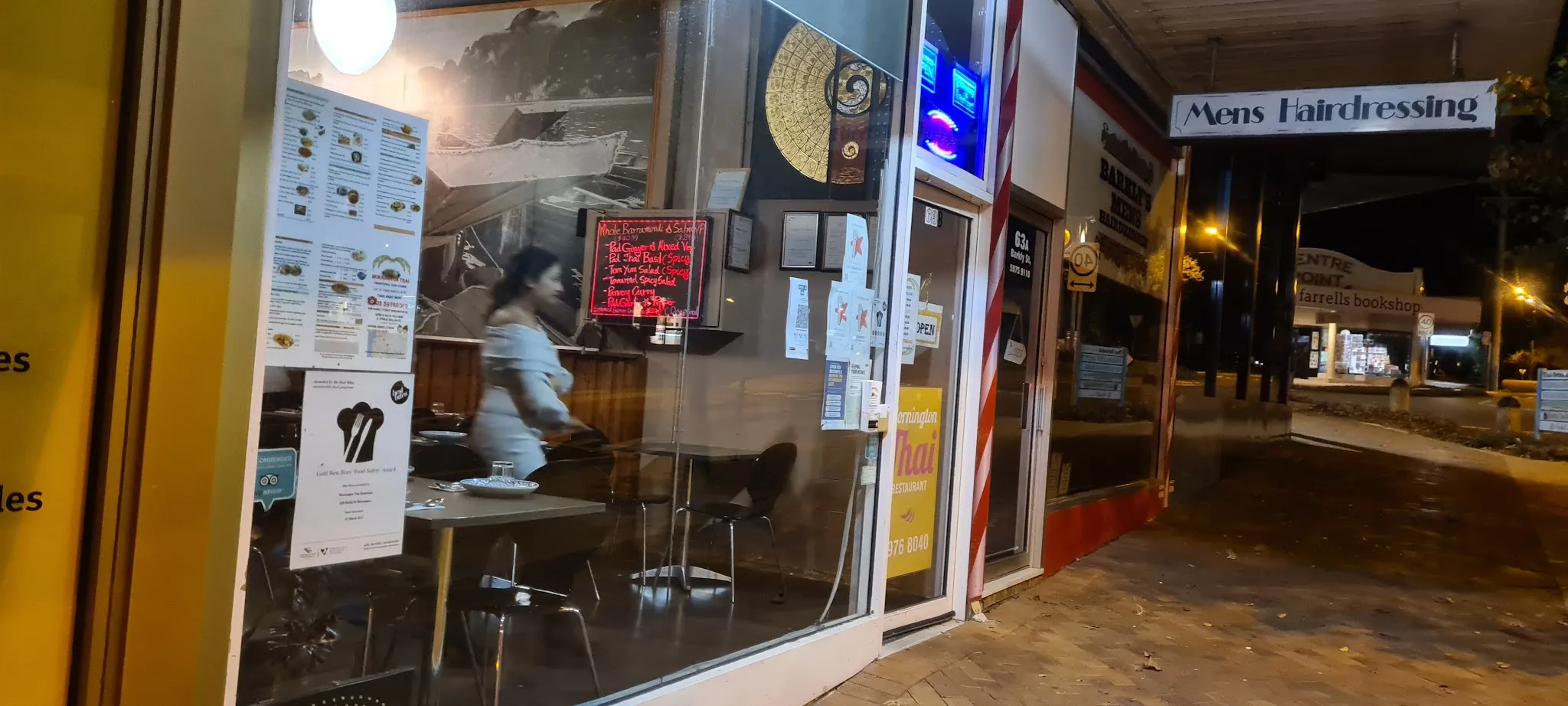 Mornington Thai Restaurant at night, warm interior glow visible through window with figure inside