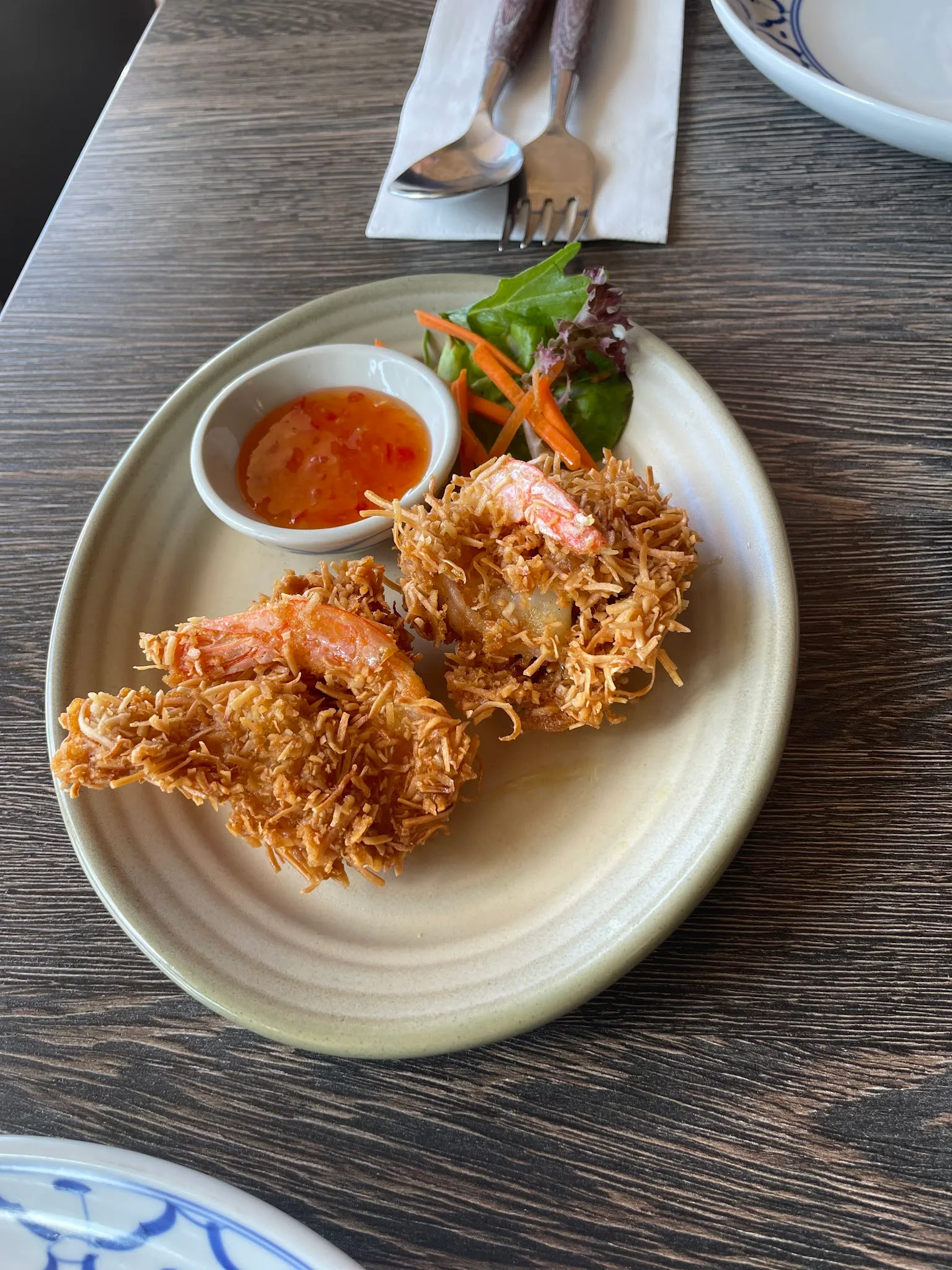 Two crispy coconut prawns with sweet chilli dipping sauce on a cream ceramic plate